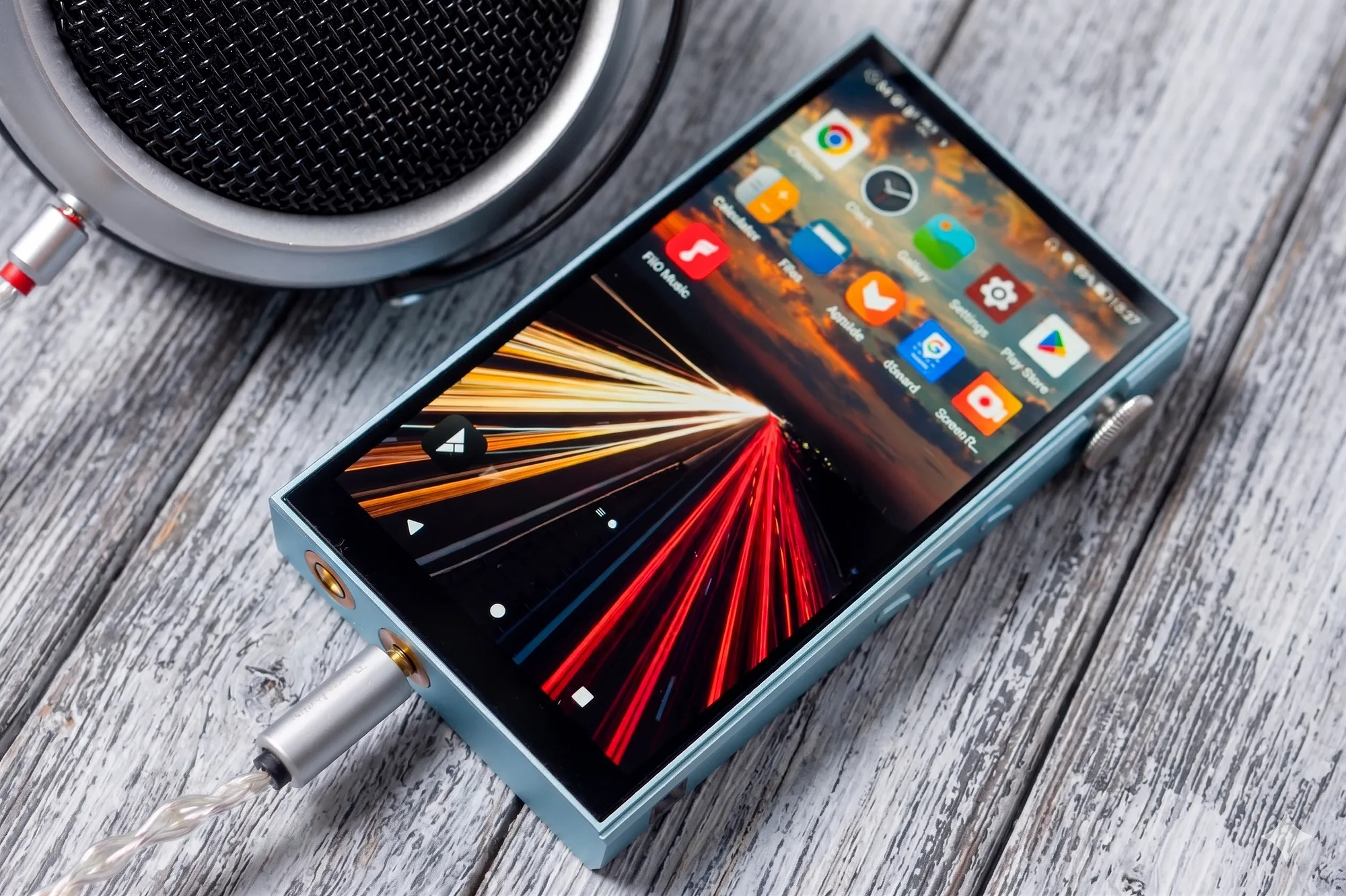 Плеер iBasso DX180 с интерфейсом Android, наушником и штекером кабеля рядом.