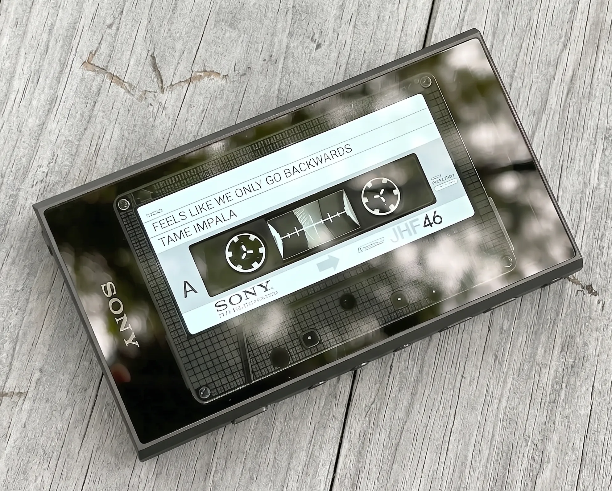 Sony NW-A306 на светлом дереве: экран с заставкой аудиокассеты, вид сверху, черный корпус.