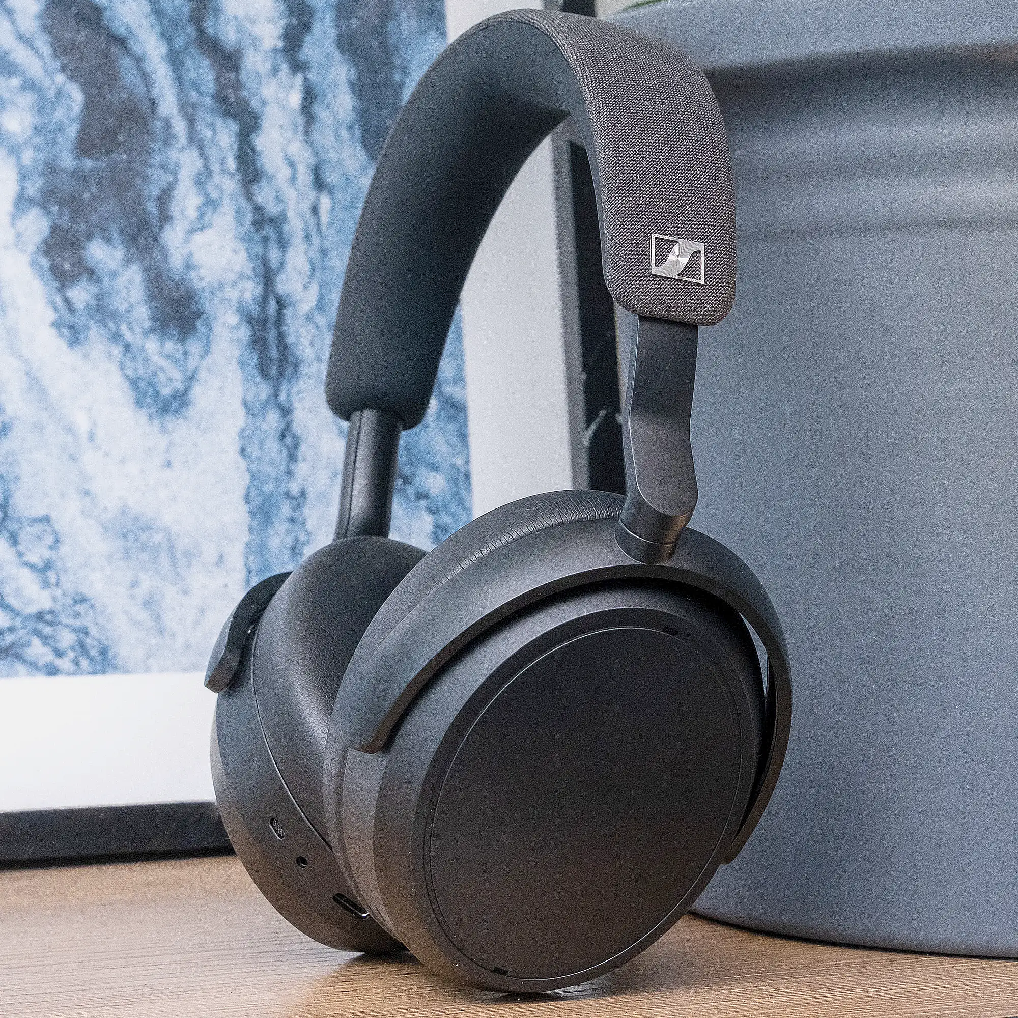 Sennheiser Momentum 4 черные на столе: оголовье с тканью прислонено к вазе, крупный план, вид сбоку.