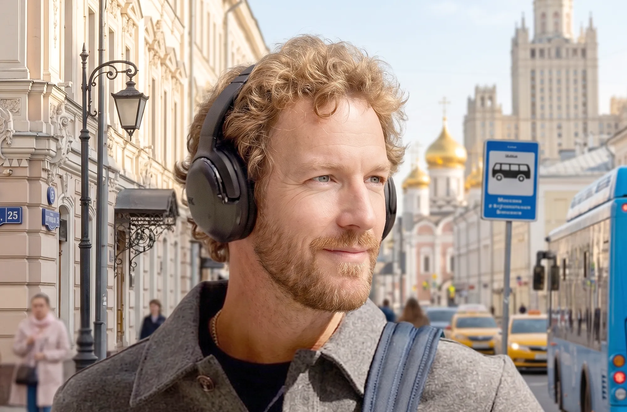 Павел Окопень в наушниках JBL Tour One M2: портрет на Пятницкой улице, синий автобус и здания, дневной свет.