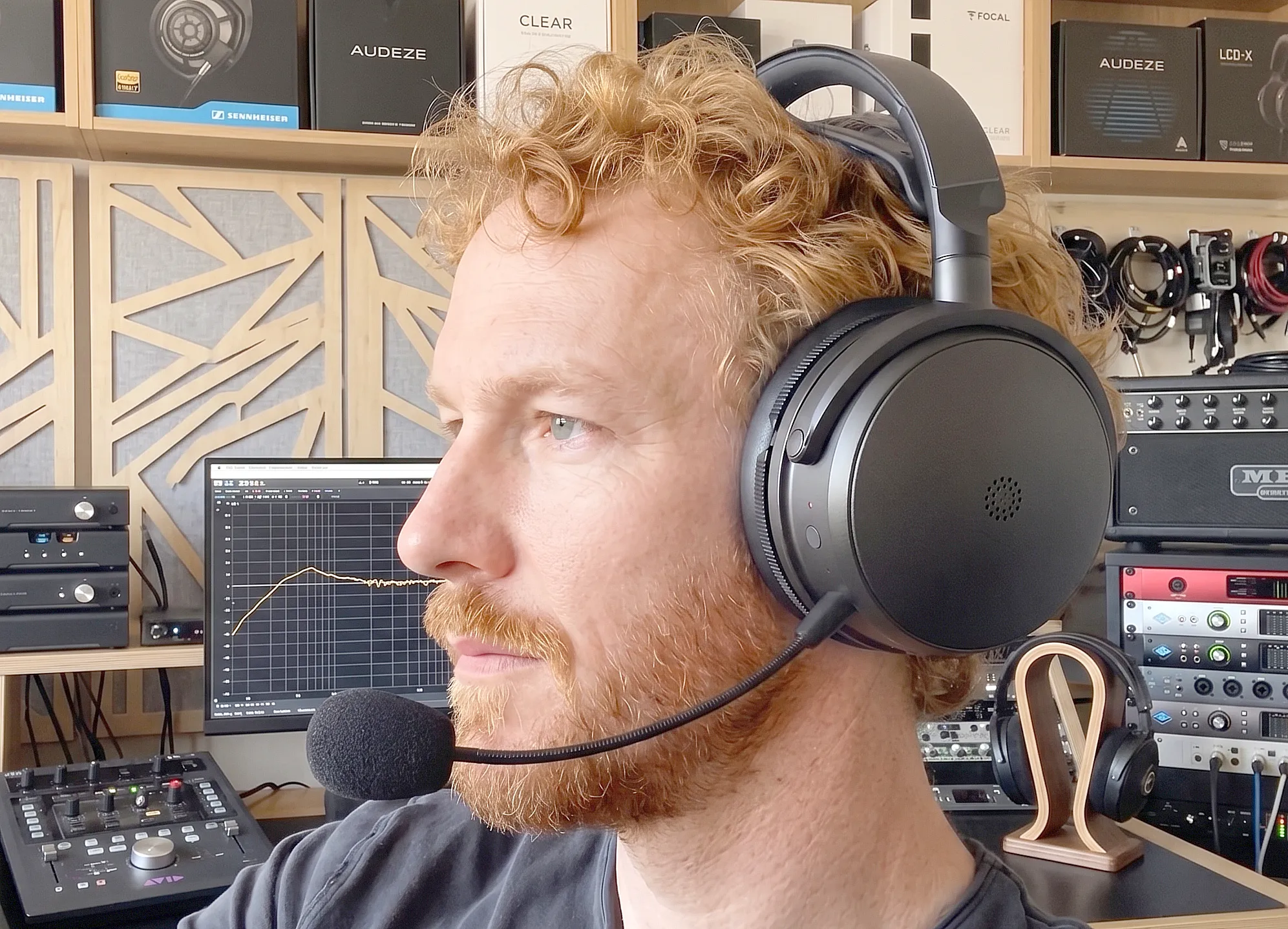 Павел Окопень в Audeze Maxwell 2: профильный портрет, черные чашки и микрофон на фоне стоек с оборудованием и коробок.