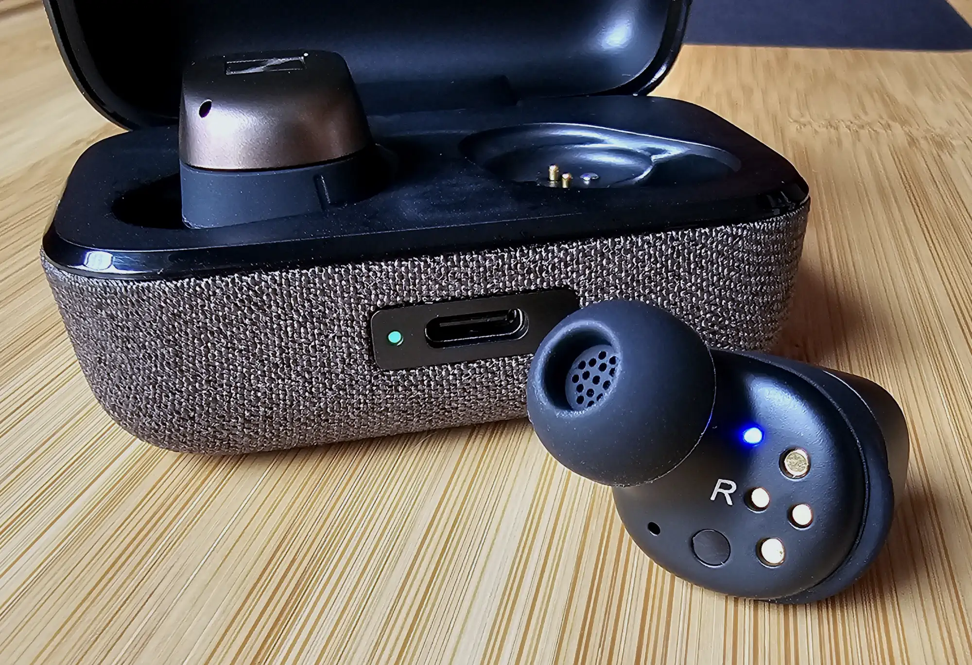 Sennheiser Momentum True Wireless 4: открытый кейс с наушником, второй на переднем плане, текстильная отделка и USB-C.