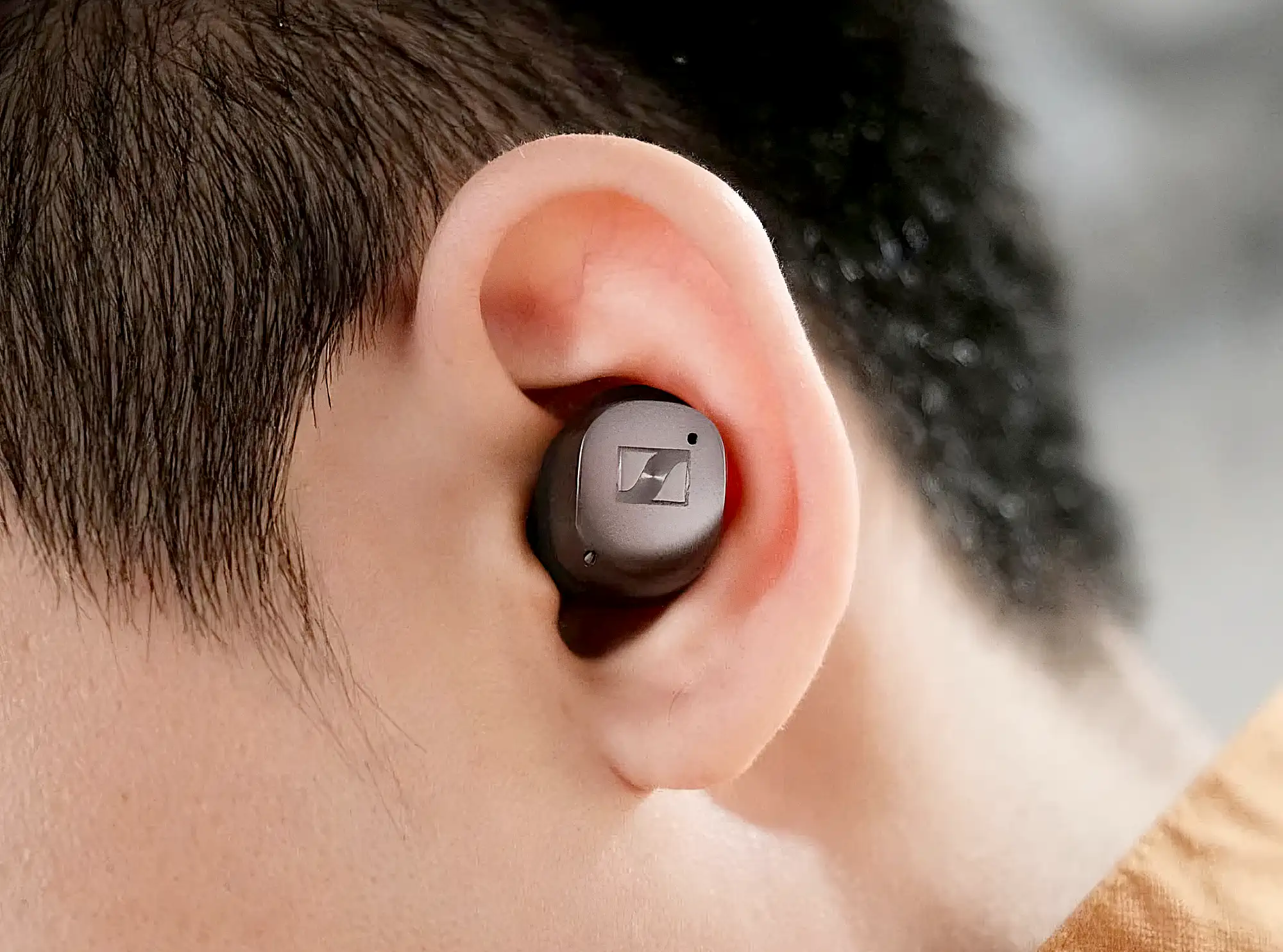 Sennheiser Momentum True Wireless 4: посадка наушника в ухе, крупный план, матовый корпус с металлизированной панелью и логотипом.
