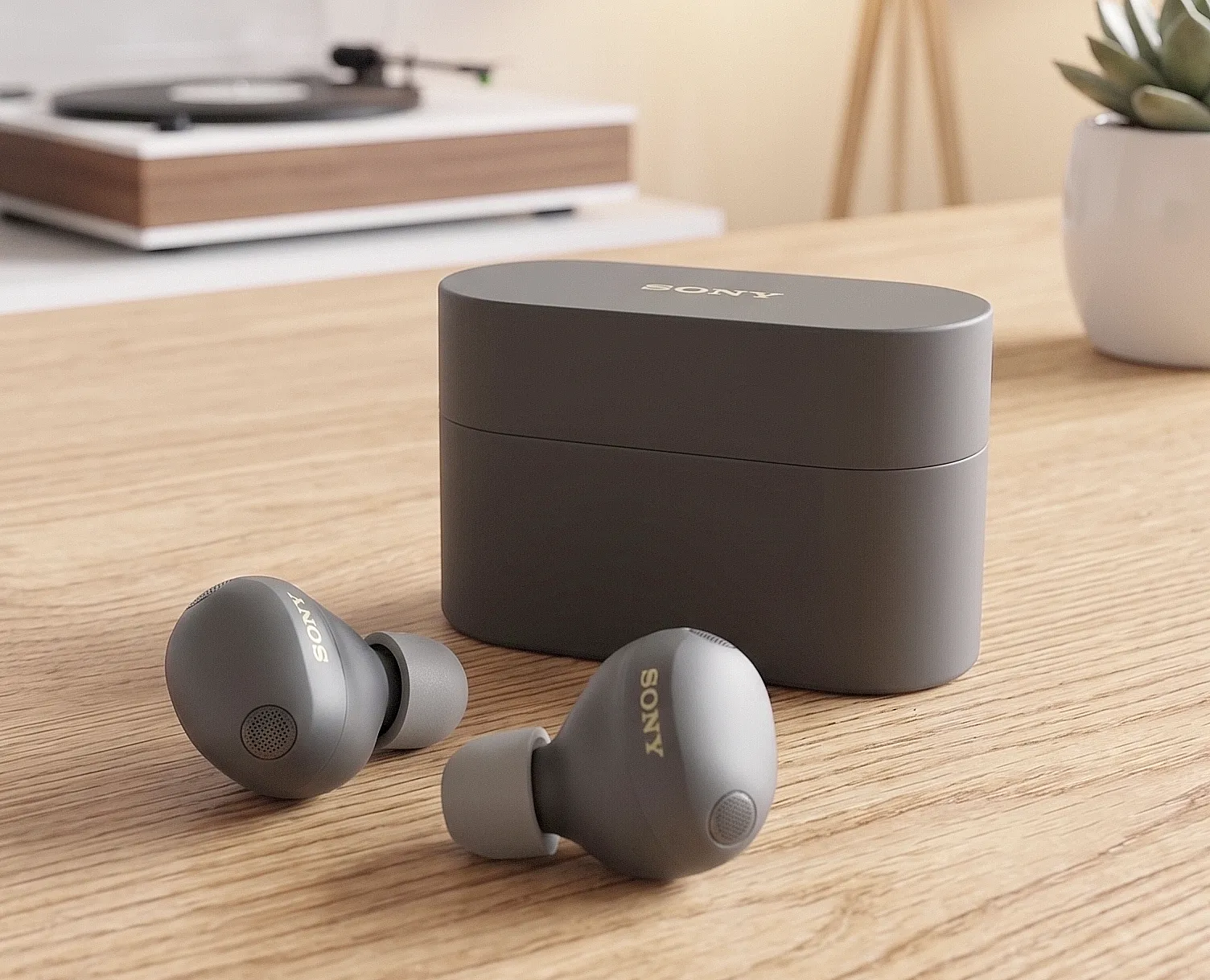 Sony WF-1000XM6: серые TWS-наушники и закрытый кейс на деревянном столе, матовый пластик и золотой логотип SONY.