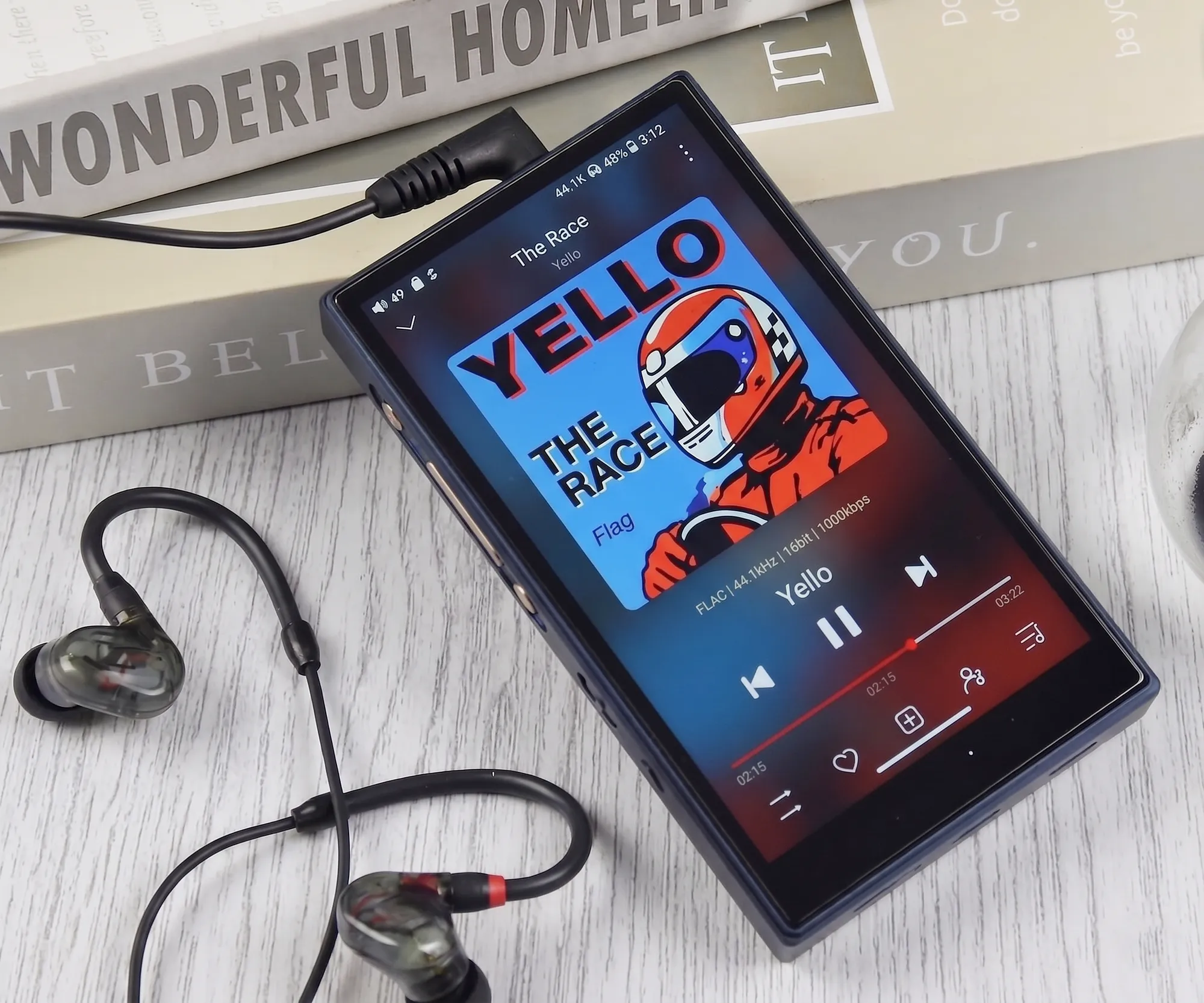 FiiO M21 на деревянном столе: диагональный ракурс, обложка трека на экране, рядом наушники.