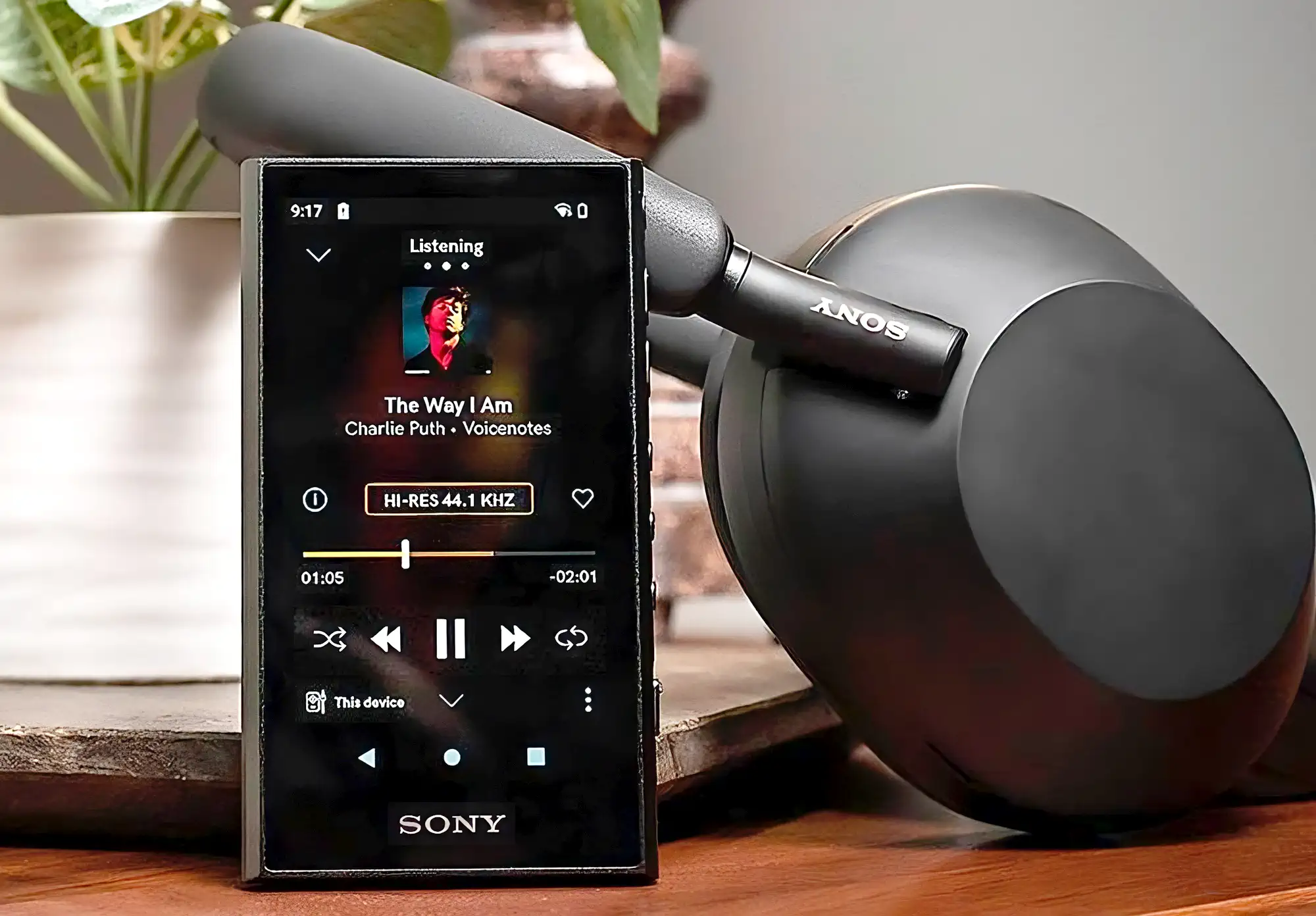 Sony NW-A306 на столе: вертикально, прямой ракурс, трек на экране, фон – черные наушники.