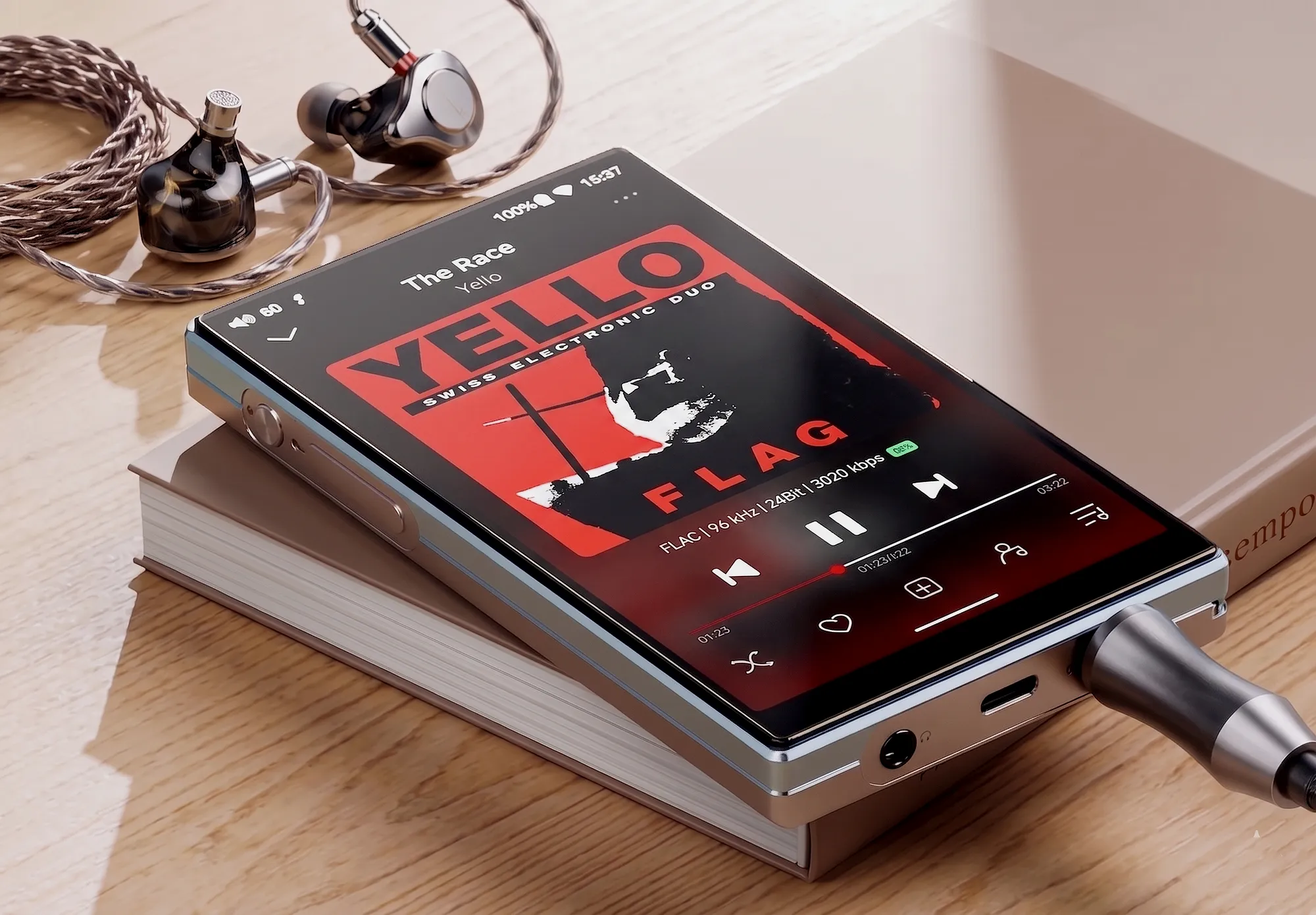 Цифровой плеер FiiO JM21 на книге – диагональный ракурс. На экране красная обложка, снизу штекер, на фоне наушники.