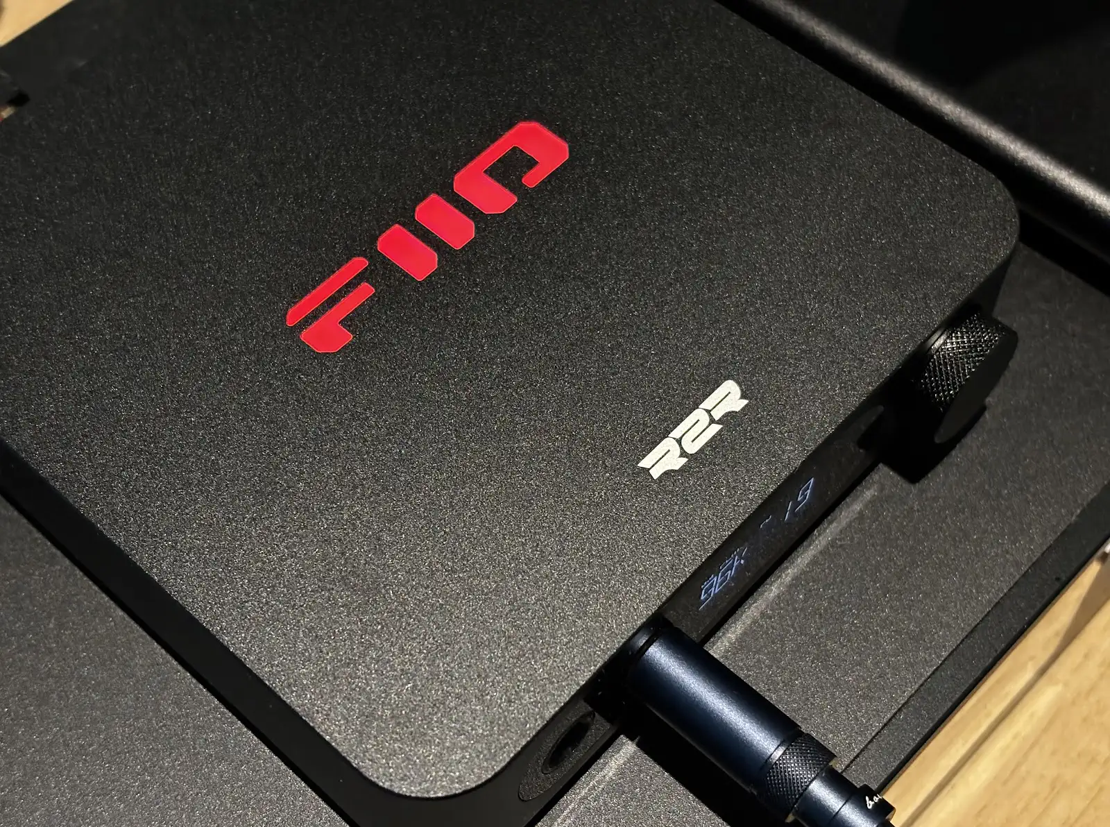 FiiO K11 R2R: крупный план матовой верхней панели с ярким светящимся RGB-логотипом по центру.