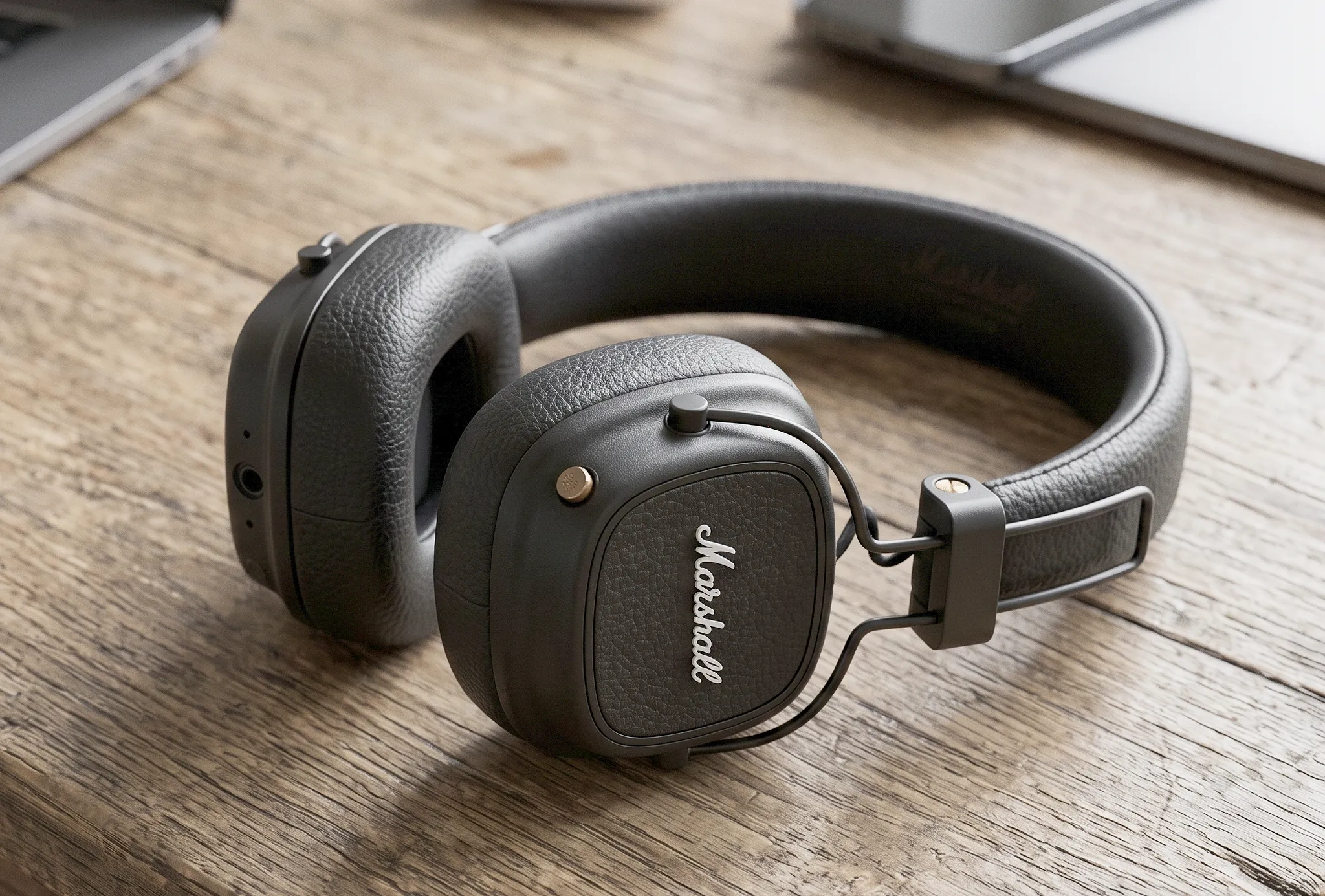 Беспроводные наушники Marshall Major V с текстурированным оголовьем, золотистым джойстиком и амбушюрами на деревянном столе.