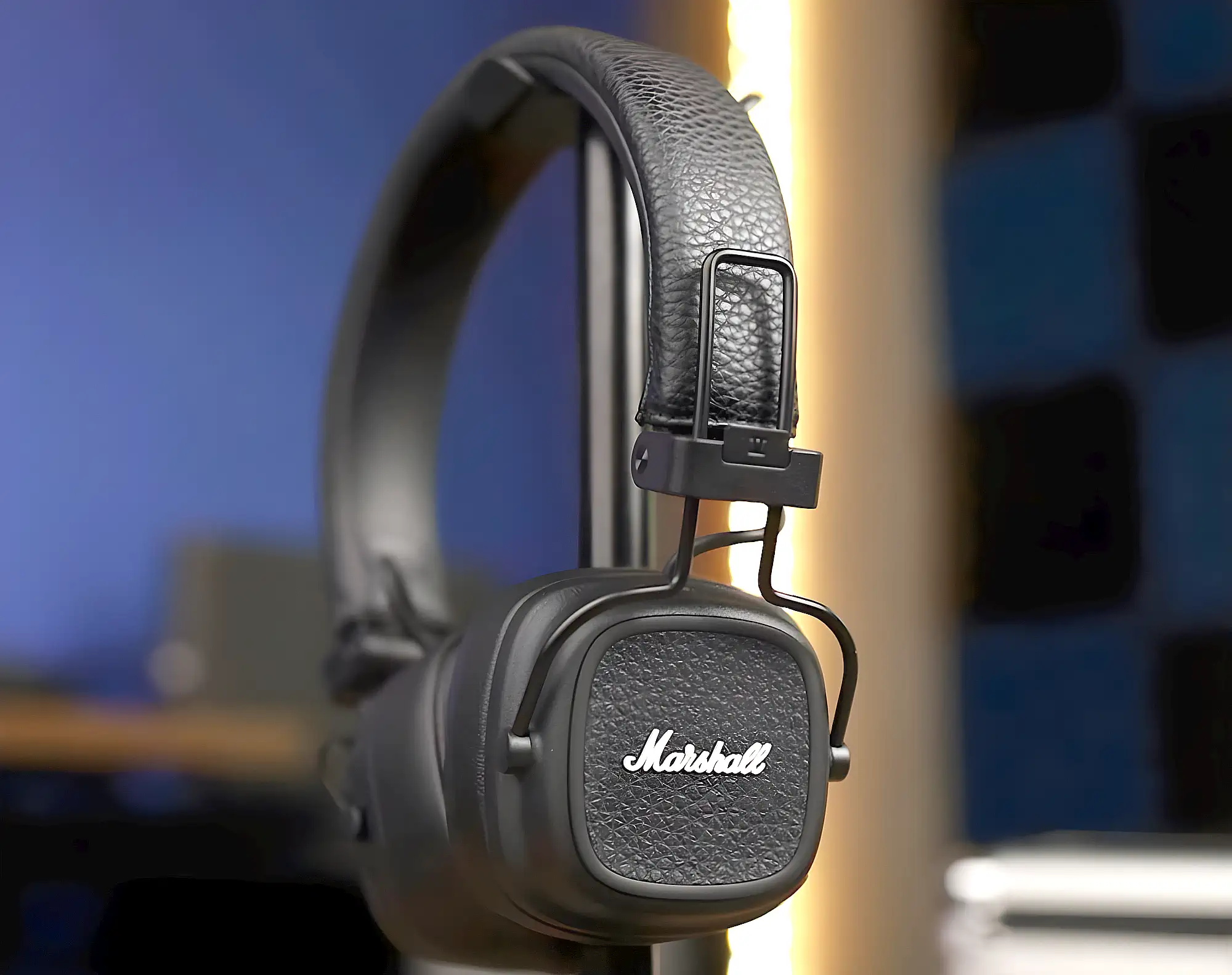 Накладные наушники Marshall Major V черного цвета на стойке. Текстурированная чашка с белым логотипом бренда крупным планом на размытом фоне.