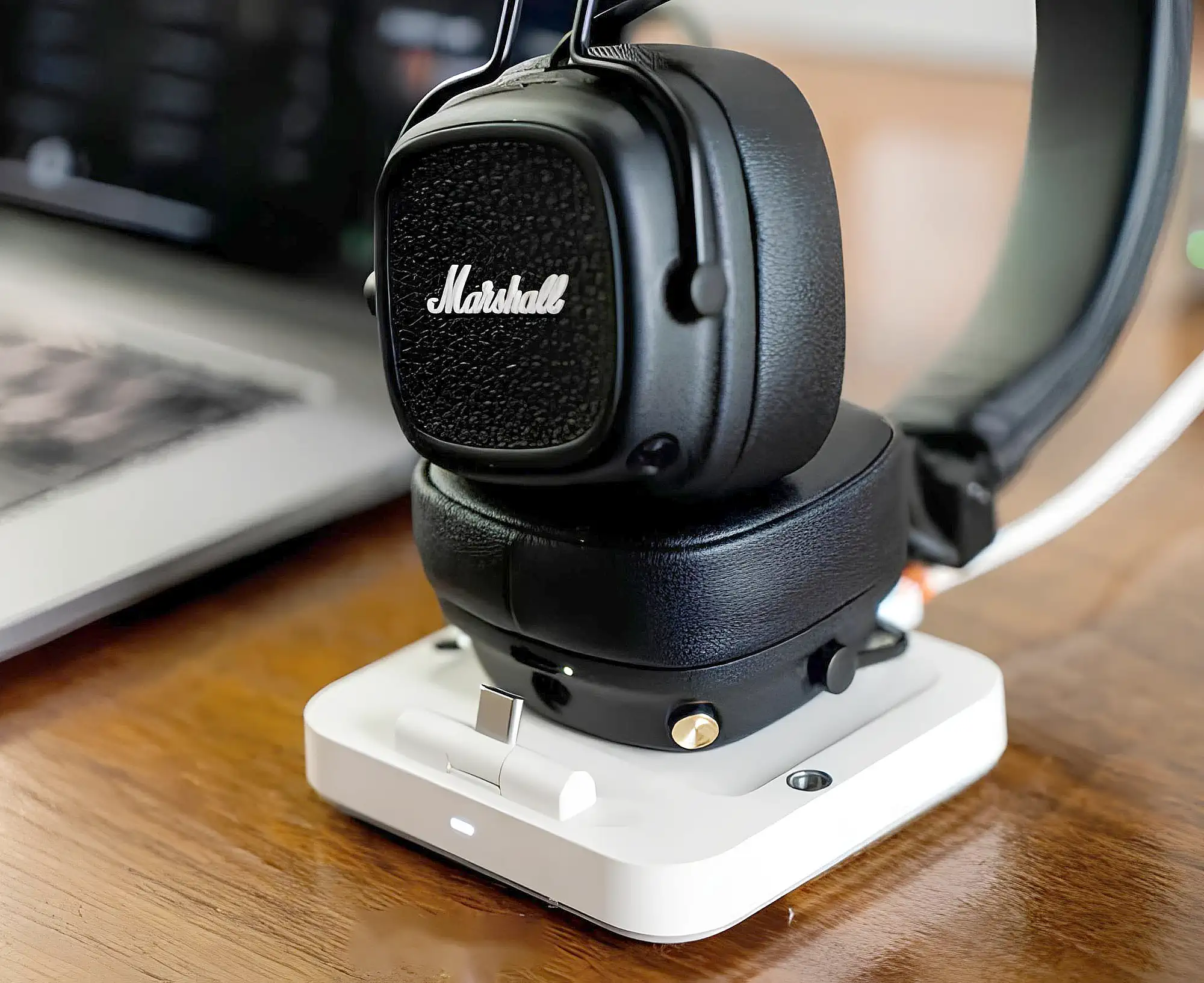 Marshall Major V: правая чашка на белой Qi-станции для беспроводной зарядки, крупный план на деревянном столе.