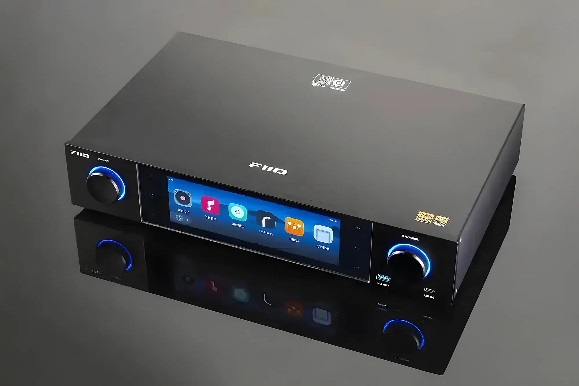 ЦАП-стример FiiO S15 на темной глянцевой поверхности с отражением. Вид сверху-сбоку, включен экран и синяя подсветка.