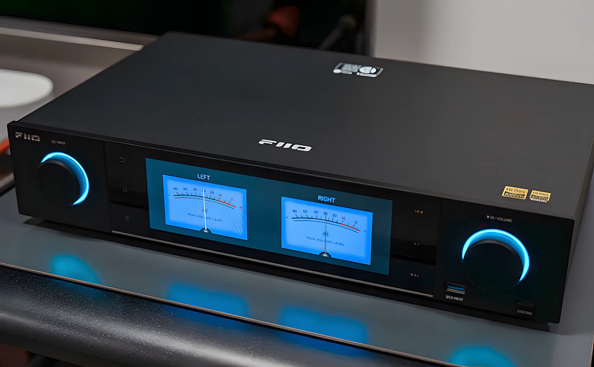 Стример FiiO S15 на столе. Вид сверху-сбоку, включен экран с синими стрелочными индикаторами.