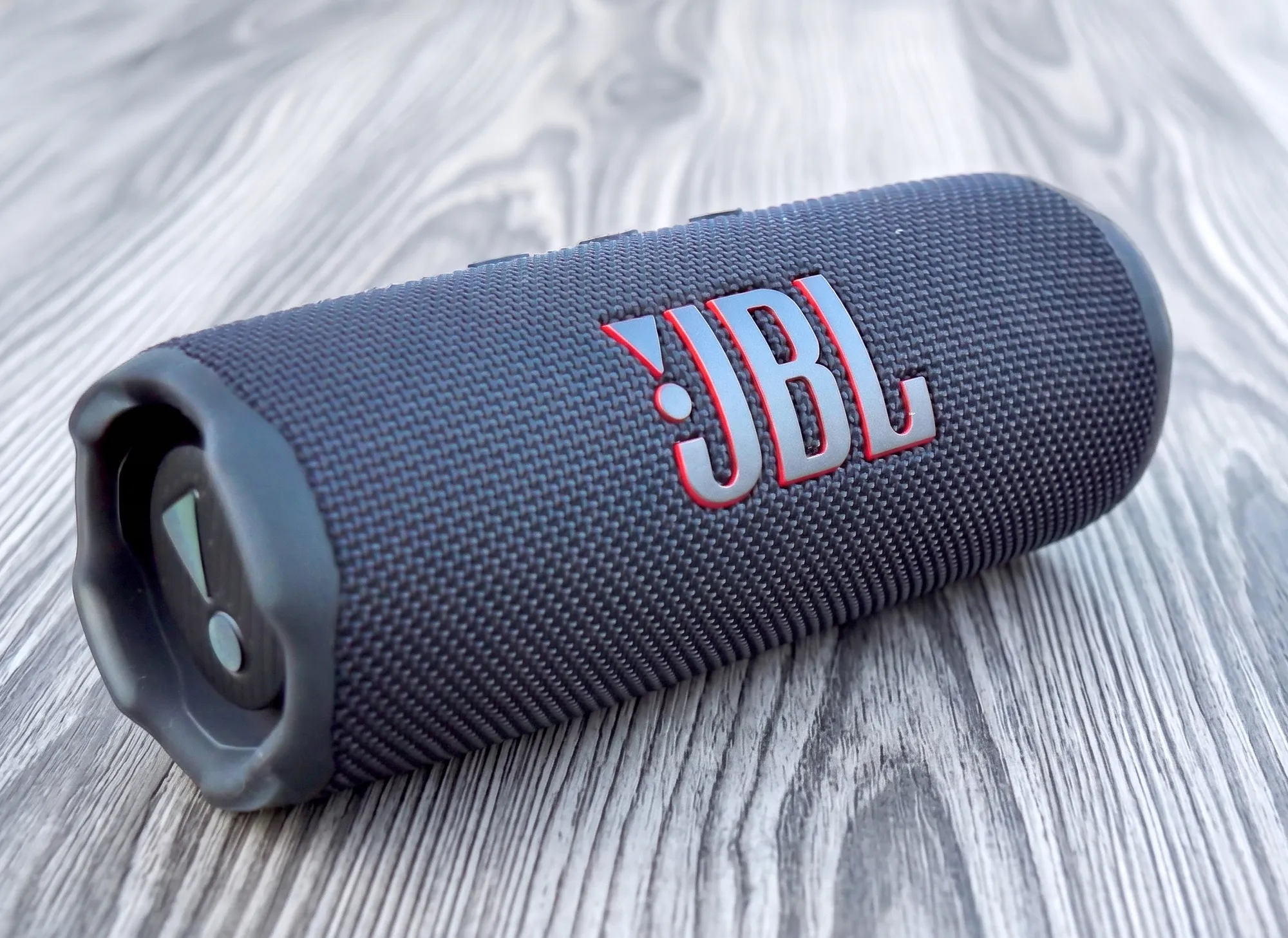 Bluetooth-колонка JBL Flip 7 черного цвета лежит на деревянной поверхности.