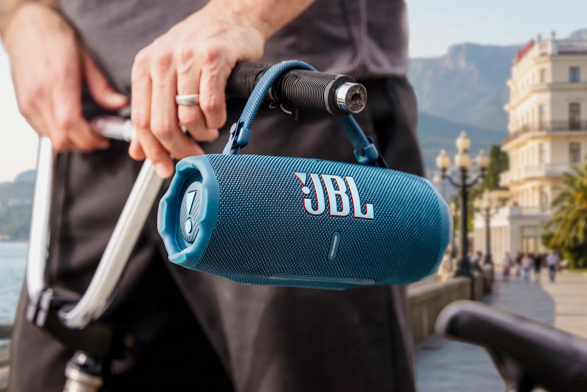 Беспроводная колонка JBL Flip 7 синего цвета закреплена на руле велосипеда. Крупный план на фоне набережной Ялты.