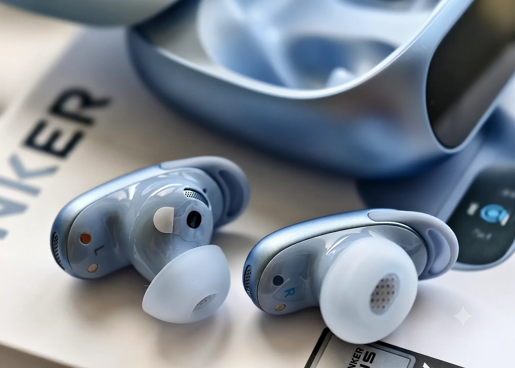 Наушники Soundcore Liberty 5 Pro рядом с открытым кейсом. Макроплан амбушюр и контактов на фоне коробки Anker.