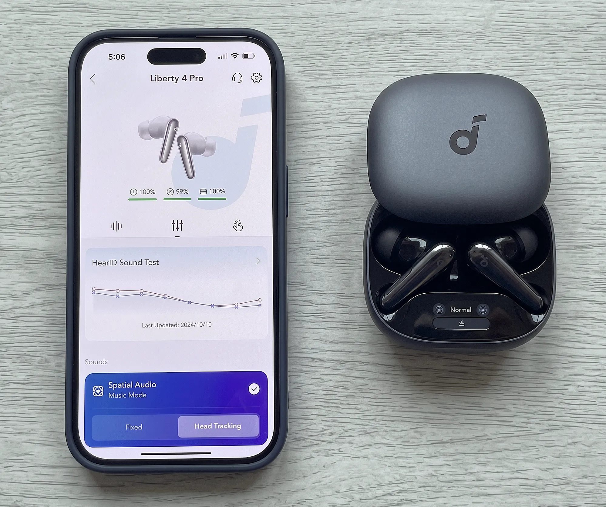 Наушники Soundcore Liberty 4 Pro рядом со смартфоном. Крупный план открытого кейса и экрана приложения.