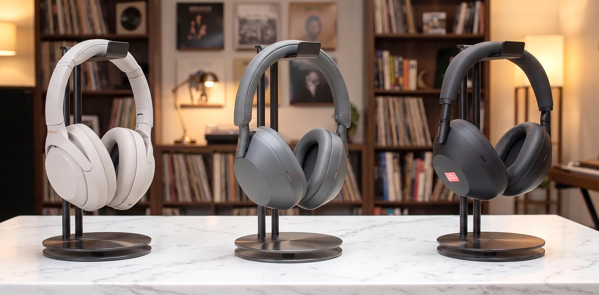 Sony WH-1000XM4, XM5 и XM6 на стойках: слева бежевые, центр серые, справа черные, фон – стеллаж с винилом.