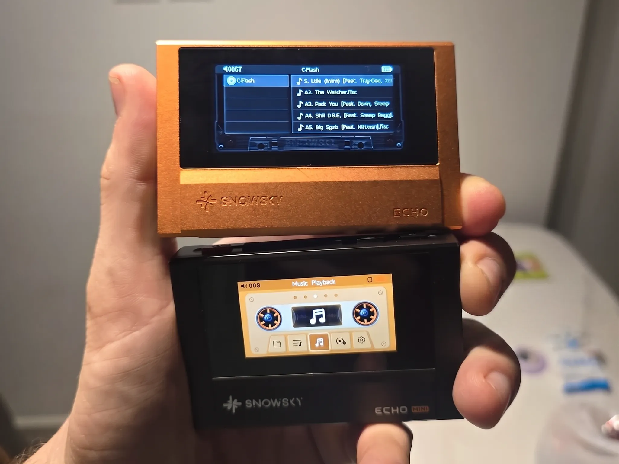 Сравнение плееров Snowsky ECHO и ECHO Mini: в руке удерживаются оранжевый корпус сверху и черный компактный снизу.