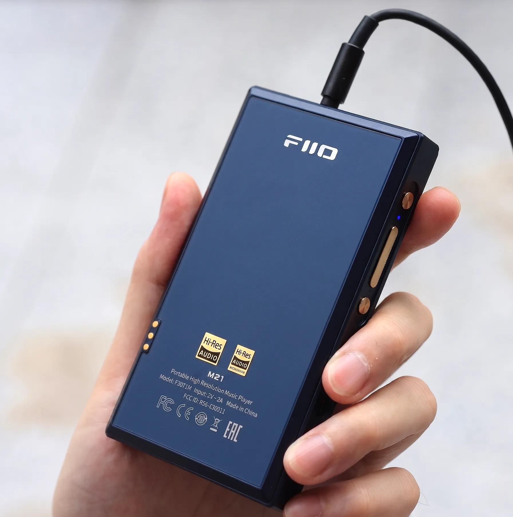 Аудиоплеер FiiO M21 в руке: задняя панель с логотипами Hi-Res Audio, кнопки сбоку и подключенный провод сверху.