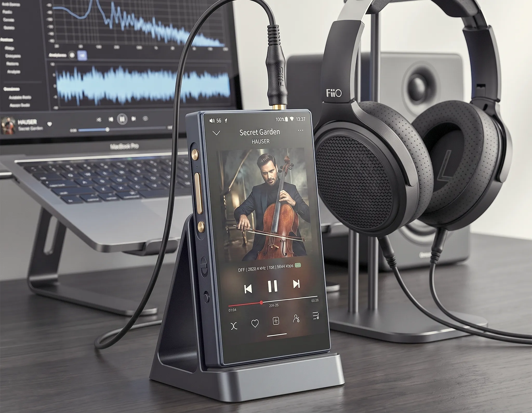 Цифровой плеер FiiO M21 на подставке: воспроизведение трека на экране, подключенный кабель, рядом ноутбук и наушники.