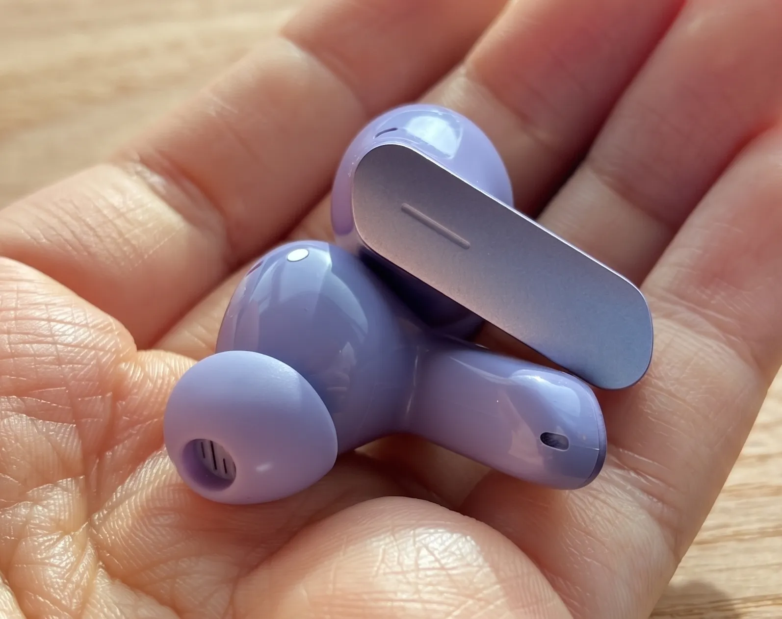 Капсулы TWS-наушников Realme Buds Air 7 на ладони: глянцевый сиреневый корпус, амбушюры и сенсорные ножки.