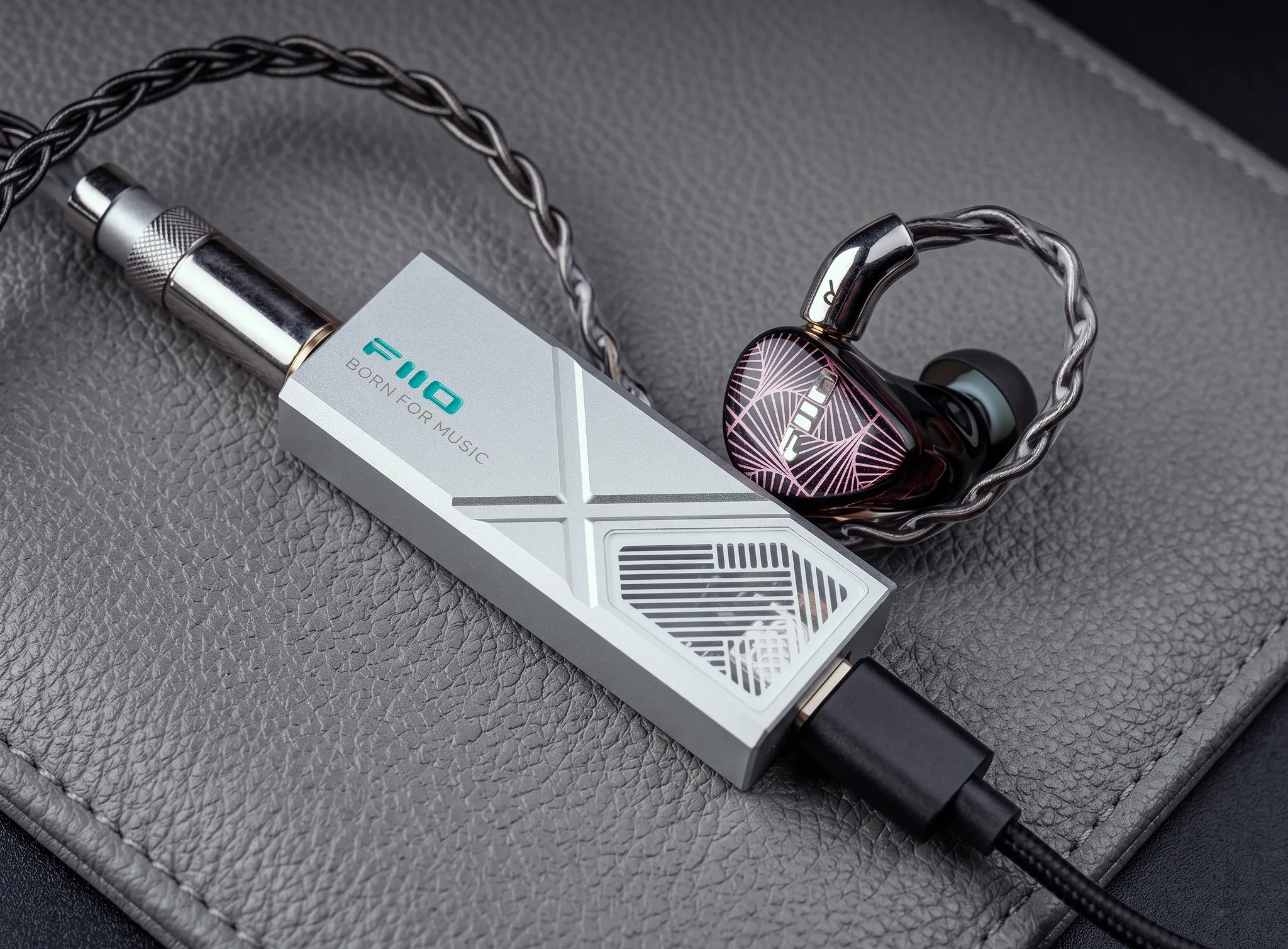 Портативный ЦАП-усилитель FiiO KA13 в серебристом корпусе с подключенным кабелем питания и внутриканальным наушником.