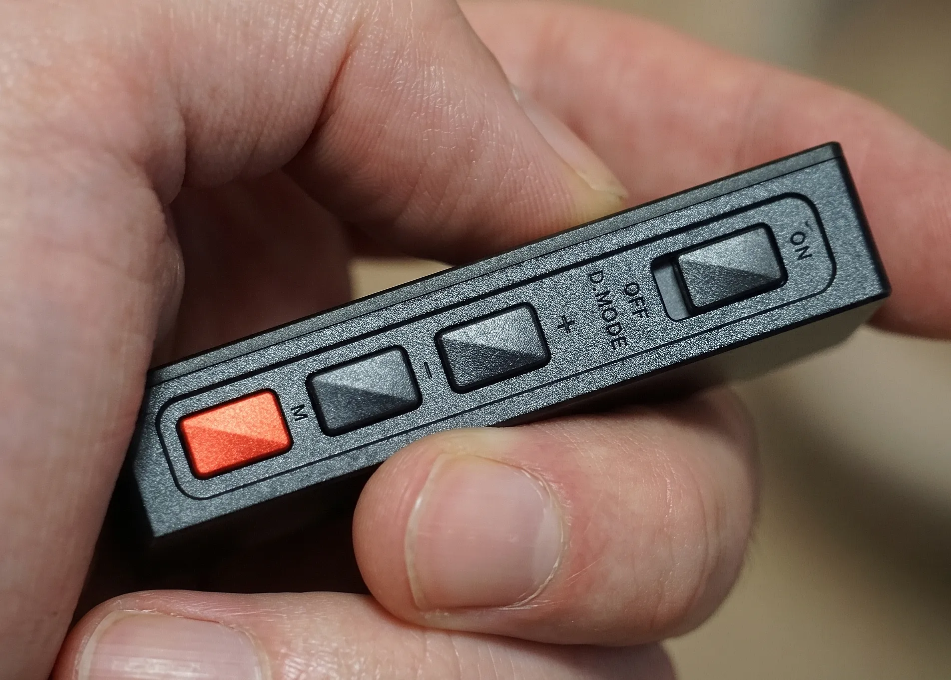 Боковая грань ЦАП-усилителя FiiO KA15 в руке: переключатель режимов Desktop Mode, качелька громкости и оранжевая функциональная кнопка меню «M».