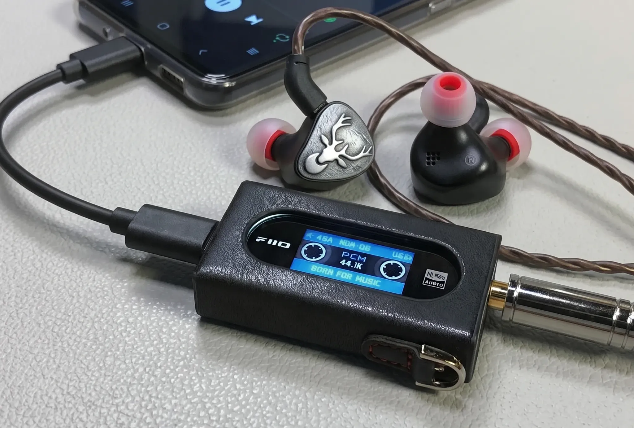 ЦАП-усилитель FiiO KA15 в черном кожаном чехле с активным экраном в связке со смартфоном и внутриканальными наушниками.
