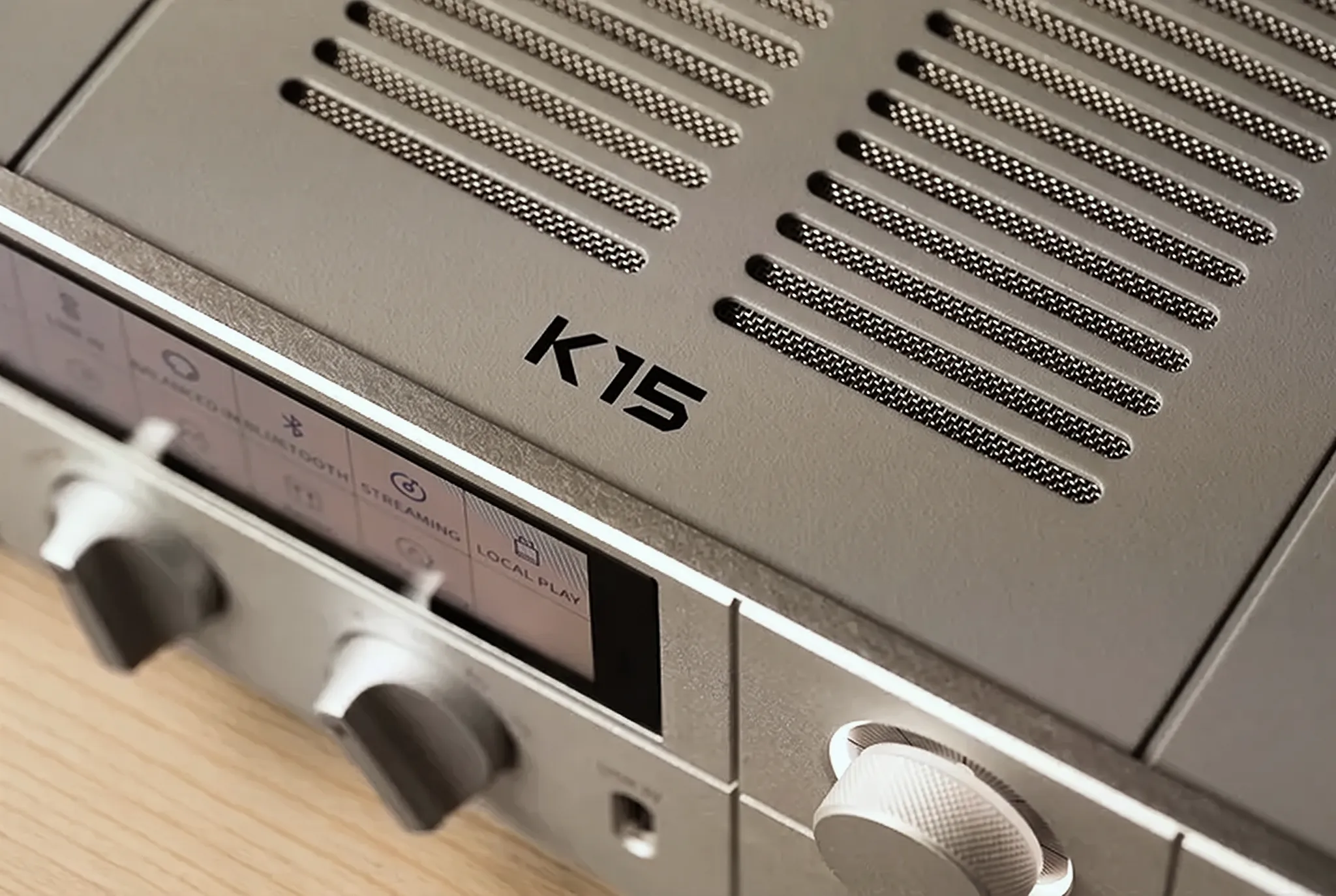 Крупный план ЦАП-усилителя FiiO K15: стык серебристой фронтальной панели и серого верхнего кожуха.