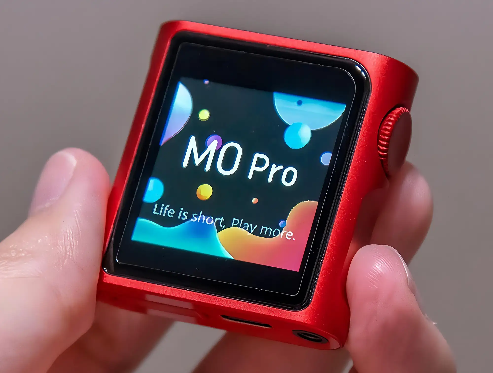 Красный аудиоплеер Shanling M0 Pro в руках. В центре – включенный дисплей с текстом «M0 Pro», справа расположено колесо управления. Крупный план.