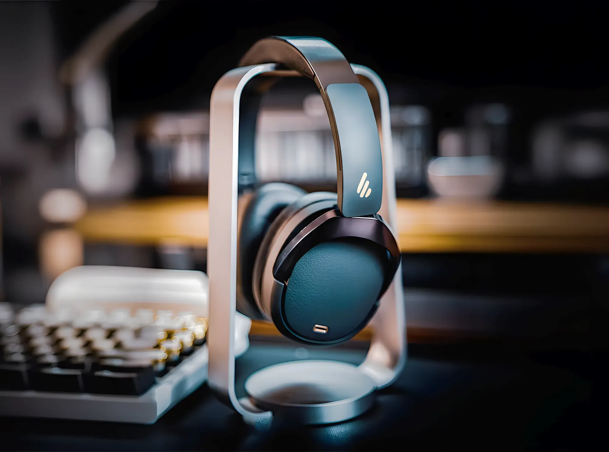 Беспроводные наушники Edifier WH950NB на настольной подставке на переднем плане, слева частично видна клавиатура, на рабочем столе